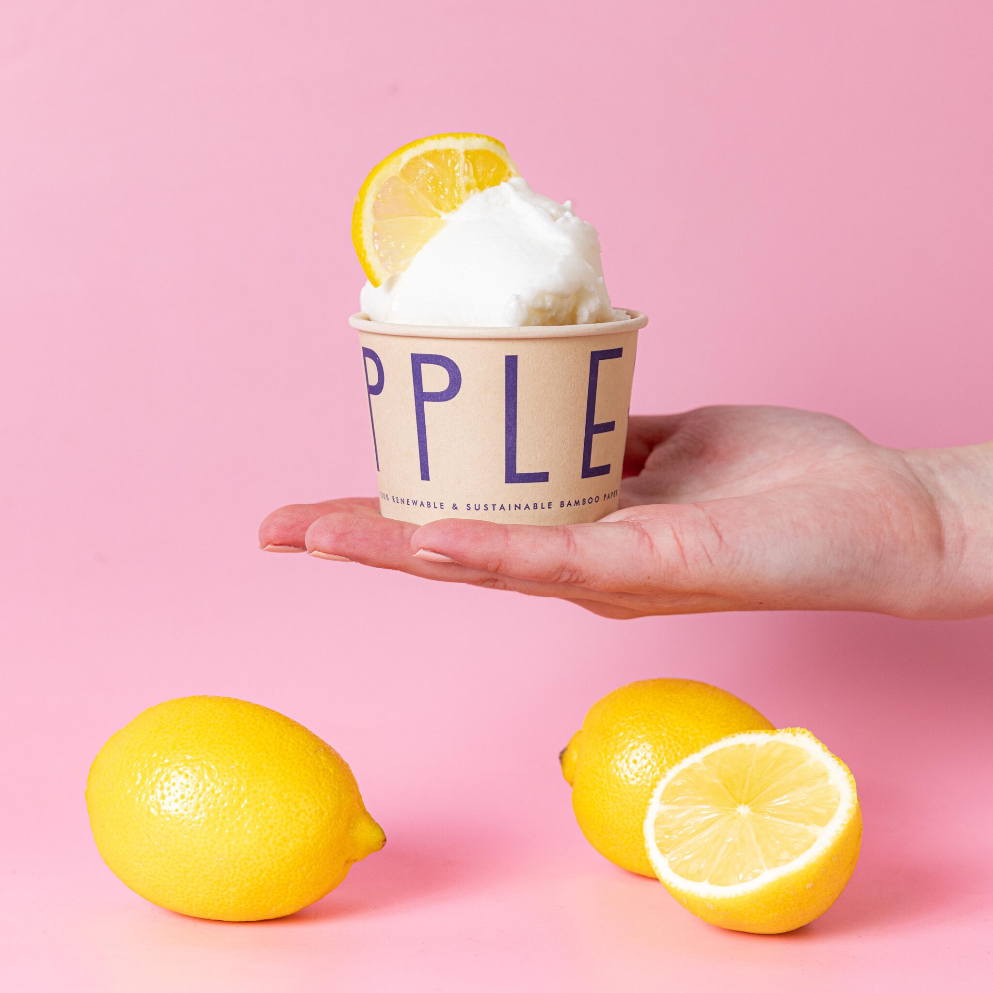 a hand hold out a lemon sorbet in a cup with lemons scattered around it