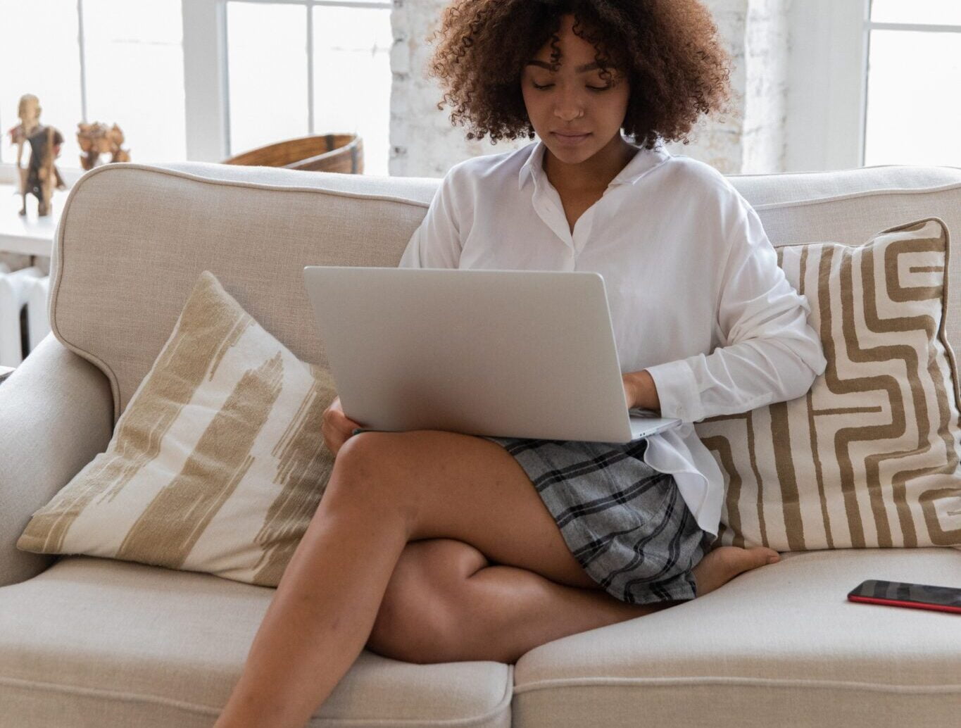 women sits on couch working on her laptop with her phone next to her